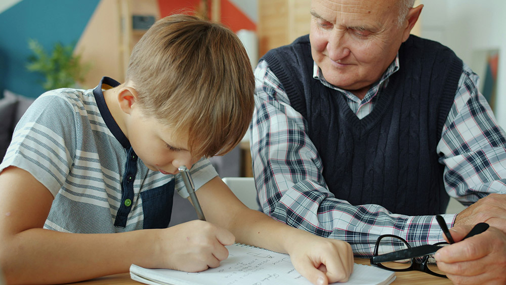 Older man watching a younger boy writing